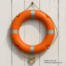 Orange MED certified lifebuoy ring with reflective tape and grab lines on white background